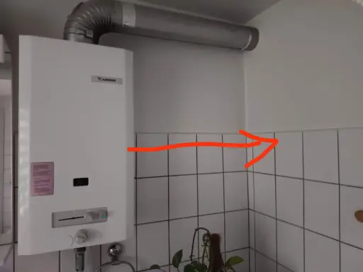 Ein Junkers-Durchlauferhitzer mit Gasflasche ist an der Wand montiert. Ein roter Pfeil zeigt auf die Ecke.