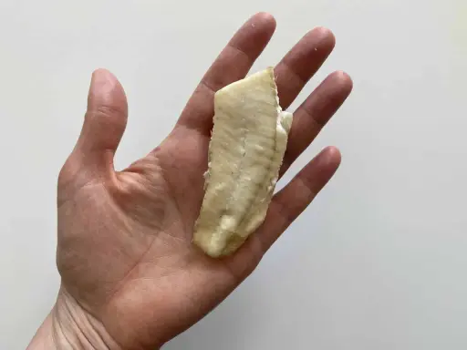 Un trozo de lenguado bebé, cocido y tierno, descansa en una mano abierta.