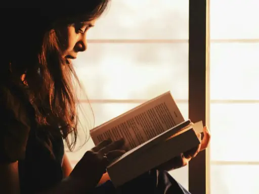 Ragazza immersa nella lettura, illuminata dalla luce dorata del tramonto, sfoglia pagine che potrebbero contenere i libri di Emmanuel Carrère.