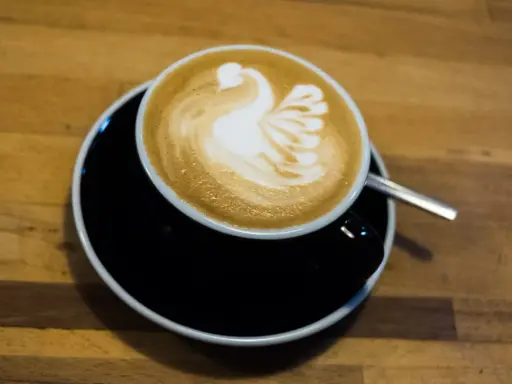Cappuccino mit Milch-Schwan-Latte-Art auf schwarzer Untertasse. Perfekt für jeden Kaffeeliebhaber.