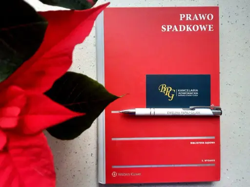 Czerwona książka "Prawo spadkowe" obok poinsecji. Długopis z nazwiskiem adwokatki i wizytówka kancelarii sugerują tematykę prawną, być może związaną z zapisem windykacyjnym.