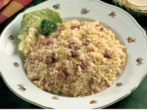 Un saporito risotto con verza e salsiccia, guarnito con una foglia di verza fresca e un ciuffo di prezzemolo.