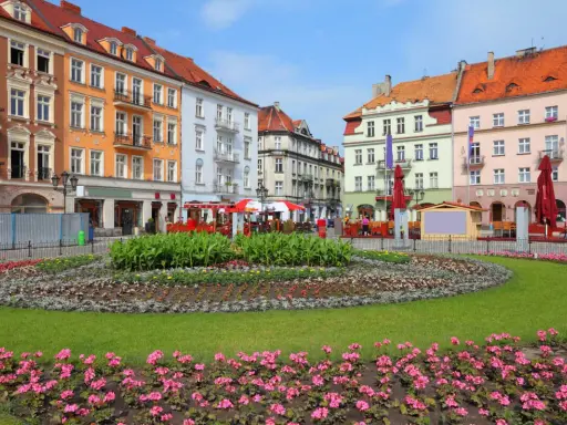 Kolorowy rynek w najstarszym mieście w Polsce, z kwitnącymi rabatami kwiatowymi i kamienicami.