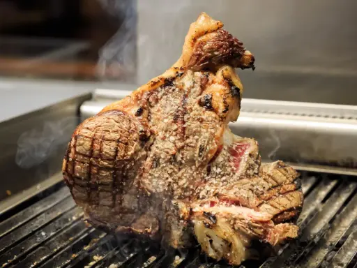 Una succulenta bistecca a Firenze, cotta alla perfezione sulla griglia, con sale grosso e fumo che sale.