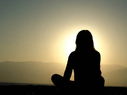 Silhuett av en person som mediterar vid solnedgången. Kanske är det en av nackdelar med meditation att man blir så fokuserad att man missar allt annat.