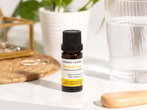 Un flacon de vitamine D3 vegan, un remède de grand-mère pour pallier le manque de vitamine D, à côté d'un verre d'eau.
