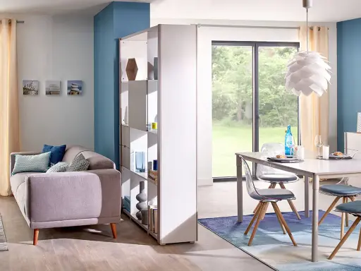 Aménagement salle à manger moderne avec canapé confortable et table design. Une étagère sépare les espaces.