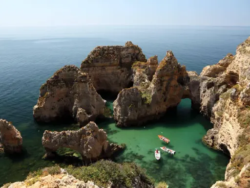 Felsformationen mit Bögen im türkisfarbenen Meer, Boote fahren vorbei. Perfektes Wetter Portugal September für einen Ausflug.