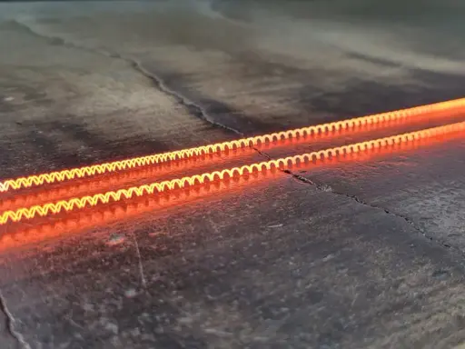 Dos espirales incandescentes, demostrando el efecto Joule en una caldera, brillan con un naranja intenso sobre una superficie oscura y agrietada.