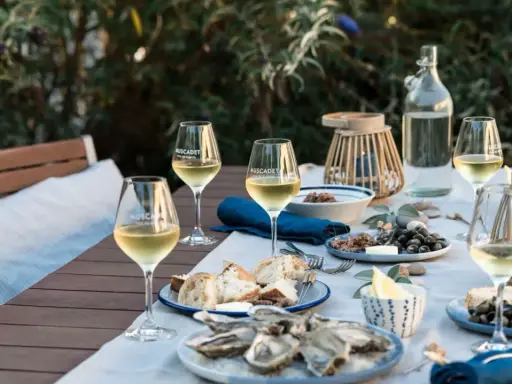 Ein gedeckter Tisch im Freien mit Austern, Brot und Gläsern voller Muscadet, einem Wein aus der Melon de Bourgogne Traube.