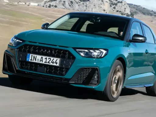 Audi RS1 verde azulado en movimiento por una carretera rural con montañas al fondo.