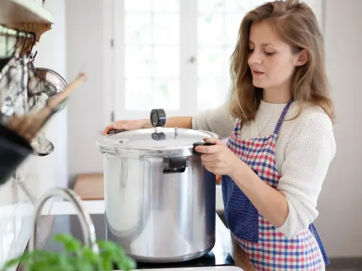 Junge Frau mit Schürze bereitet gebratenes Fleisch zum Einkochen in einem Schnellkochtopf vor.