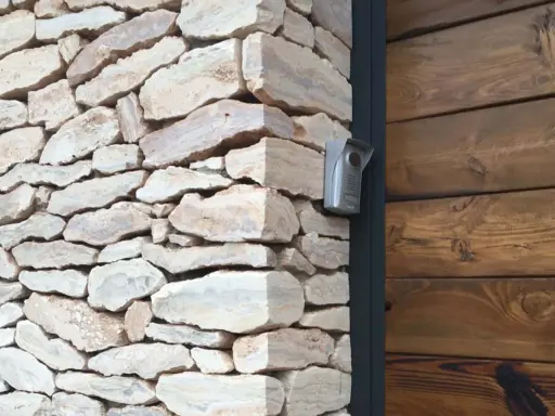 Mampostería concertada de piedra natural con un intercomunicador plateado en la esquina, junto a una pared de madera oscura.