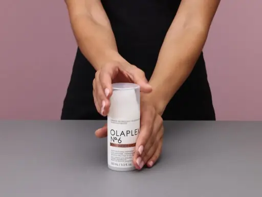 Hände halten eine Flasche Olaplex Nr. 6 Bond Smoother, ein Leave-in Styling Treatment für Feuchtigkeit und Stärke.