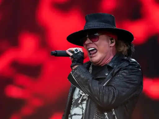 Axl Rose sjunger med en röd bakgrund. Trots rykten om axl rose sjukdom, levererar han en energisk show.