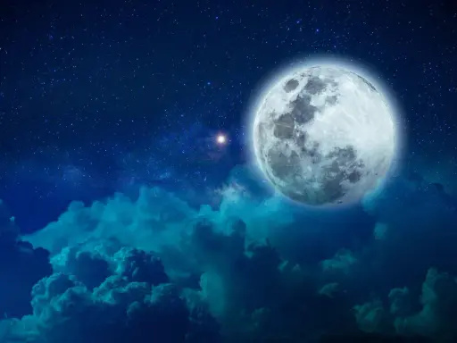 Pełnia księżyca w Byku, otoczona gwieździstym niebem i ciemnymi chmurami, tworzy magiczny widok.