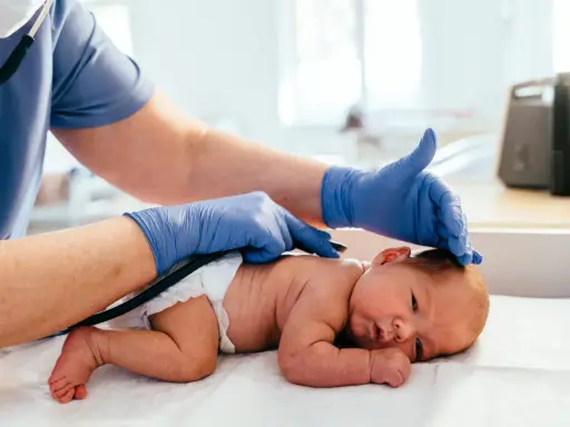 Medico controlla la schiena di un neonato, notando una piccola fossetta sacrale.