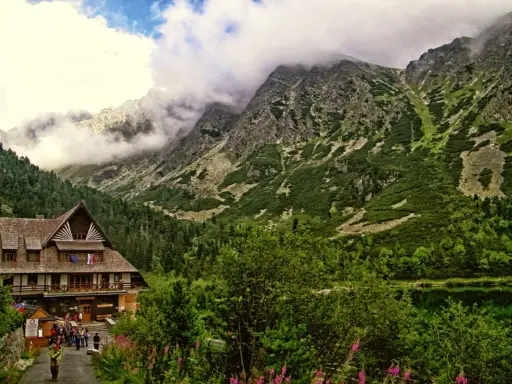 Drewniany budynek schroniska tatry w otoczeniu zielonych zboczy i skalistych gór, nad spokojnym jeziorem.