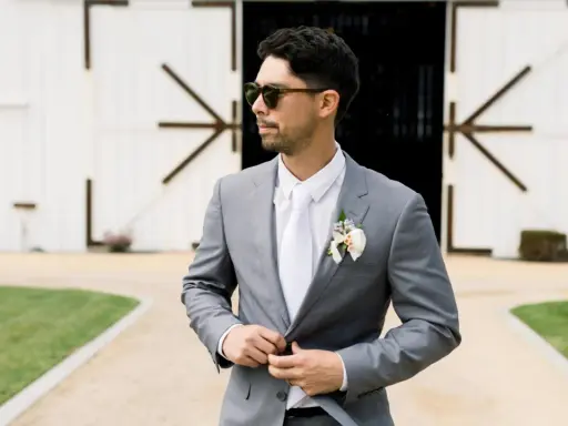 Man in a grey suit, white shirt, and tie, looking cool in sunglasses. Perfect for casual men's wedding guest attire in summer.