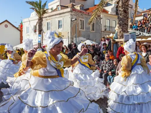 Menschen in Portugal feiern ausgelassen. Frauen in prachtvollen weißen und goldenen Kleidern mit Rüschen tanzen fröhlich.