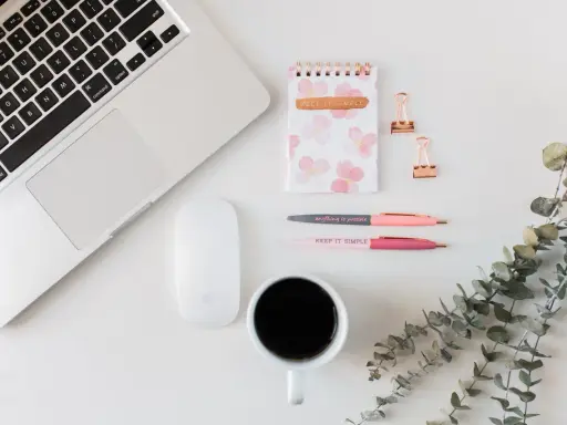 Ein Schreibtisch mit Laptop, Maus, Notizbuch, Stiften und Kaffee. Ideal für Lehrer, die ihr Zeitmanagement verbessern wollen.