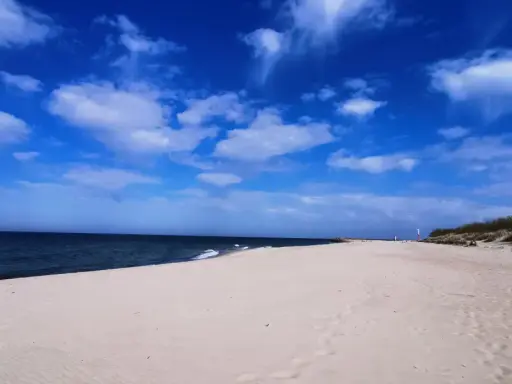 Pusta plaża z wydmami i latarnią morską, idealna na weekendowe odkrywanie magicznych miejsc nad Bałtykiem.