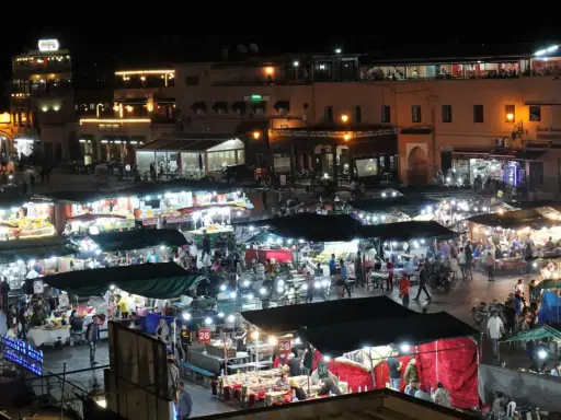 Belebter Marktplatz in Marokko bei Nacht. Viele Stände mit Lichtern und Menschen, die einkaufen und essen. Wann ist Ramadan in Marokko?