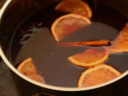 Une marmite remplie d'un liquide sombre, avec des tranches d'orange, un bâton de cannelle et de l'anis étoilé. Parfait pour une recette punch simple et réconfortante.