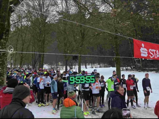 Läufer warten am Start-Ziel-Bogen für einen ultra marathon. Eine digitale Uhr zeigt 9:59:55.