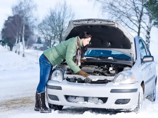 Kobieta w zimowej kurtce sprawdza silnik samochodu na śniegu. Zastanawia się, w jakiej temperaturze zamarza diesel, by uniknąć problemów.
