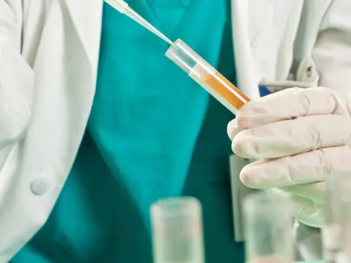 Badacz w białym fartuchu i rękawiczkach pobiera próbkę płynu do probówki. Badanie może pomóc ustalić, jak zahamować krwiomocz.