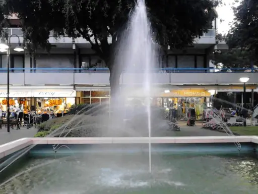 Fontana z fontanną w centrum Lido di Savio, z widokiem na sklepy i drzewa.