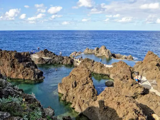 Naturschwimmbecken auf Madeira, umgeben von vulkanischem Gestein, mit Menschen, die die Sonne und das Meer genießen.