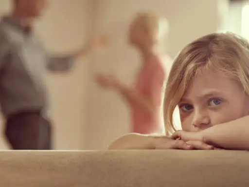 Niña asustada, escondida tras un sofá, mientras sus padres discuten delante de los hijos.