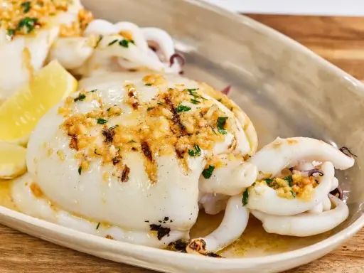 Delicioso sepia a la plancha con ajo, perejil y limón, servido en una bandeja.