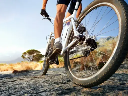 Kolarz na rowerze crossowym lub trekkingowym pokonuje kamienistą ścieżkę w słoneczny dzień.