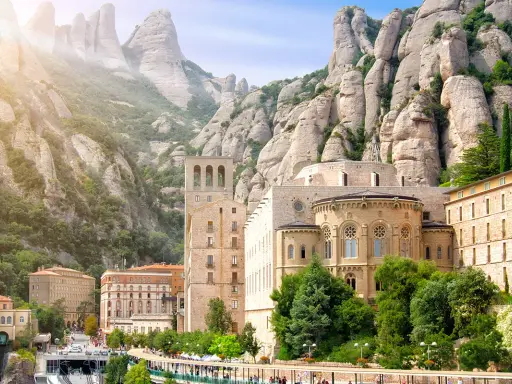 Klasztor Montserrat wznosi się wśród skalistych szczytów, z budynkami o architekturze przypominającej czcionkę Montserrat.
