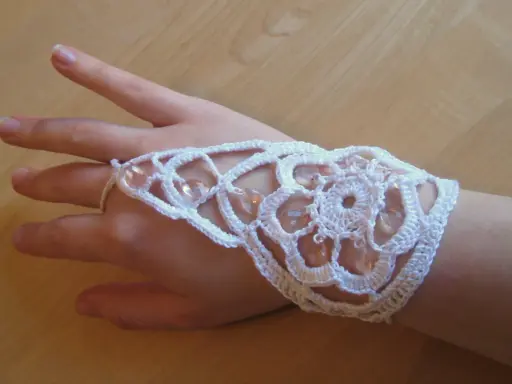 Ett vackert virkat armband i vitt med pärlor, som pryder en hand.