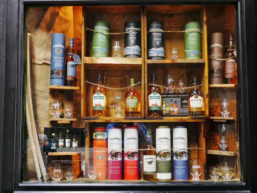 Regale voller irischer Whiskeys, darunter Connemara peated whisky, Kilbeggan und Tyrconnell. Gläser und Flaschen sind kunstvoll arrangiert.