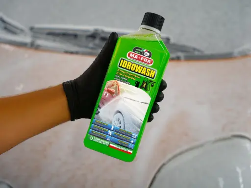 Mano con guanto nero tiene bottiglia di Idrowash, un detergente schiumoso verde brillante per auto.