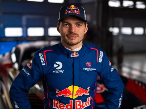 Max Verstappen im Rennanzug, bereit für das 24h Rennen. Sein Blick ist fokussiert, die Red Bull-Logos sind deutlich sichtbar.