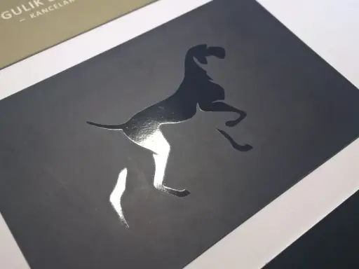 Elegancka wizytówka z psem w skoku, wykonana techniką lakierowania wybiórczego. Błyszczący pies kontrastuje z matowym tłem.
