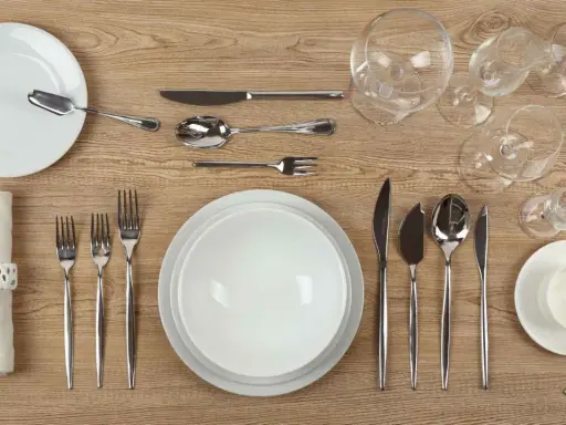 Une table dressée avec un **caractère élégant** : assiettes blanches, couverts en argent, verres à pied et une serviette décorée.