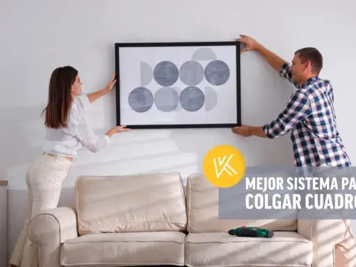 Pareja cuelga un cuadro moderno en pared de pladur. Un taladro descansa sobre el sofá, listo para la tarea.