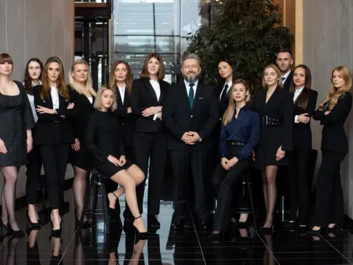 Grupa prawników i adwokatów w eleganckich strojach pozuje do zdjęcia w nowoczesnym wnętrzu.