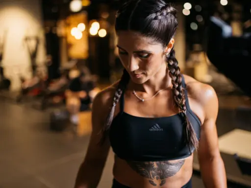 Frau mit geflochtenen Haaren im Fitnessstudio, die ihre definierten Muskeln zeigt.
