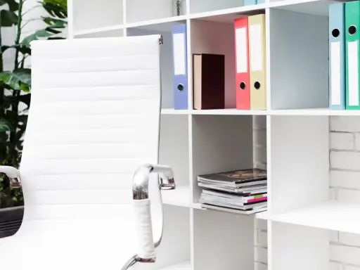Scrivania ordinata con sedia bianca e scaffali pieni di raccoglitori colorati, perfetti per chi cerca idee su come organizzare i documenti di casa.