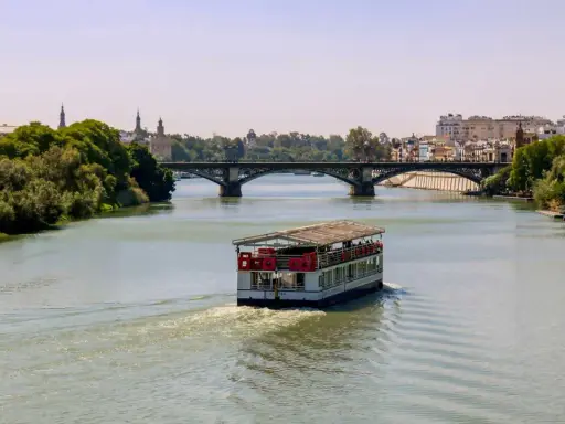 Ein Ausflugsboot fährt auf dem Guadalquivir, dem sevilla fluss, unter einer Brücke hindurch.