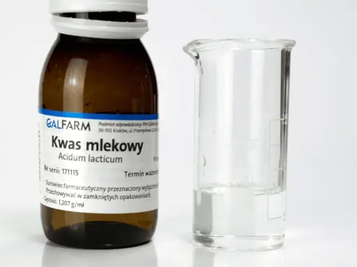 Butelka z napisem "Kwas mlekowy" i zlewka z płynem. Czy kwas mlekowy jest szkodliwy? Zależy od stężenia i zastosowania.