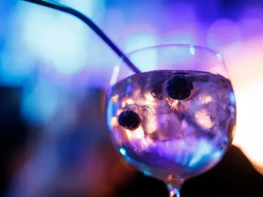 Ein Glas mit Eis und Beeren, in dem das tonic water leuchtet, vor einem verschwommenen, bunten Hintergrund.